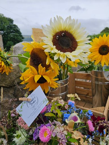 A selection of sunflowers with bumblebees and a garden-gathered posy of flowers with a business card attached.  